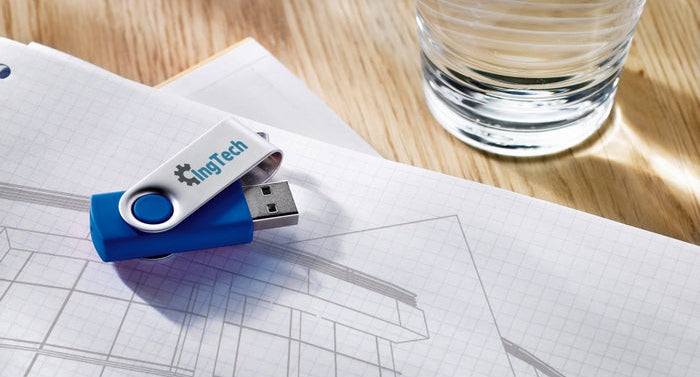 A blue and silver USB flash drive with the brand name 'HngTech' printed on it, resting on a sheet of graph paper next to a glass of water on a wooden table.