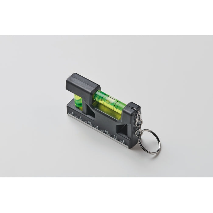 A black and gray spirit level keychain tool with a clear green liquid bubble and a metal split ring, shown on a light gray background.
