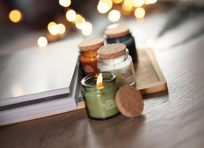 Candle with cork lid on a wooden surface with blurred lights in the background
