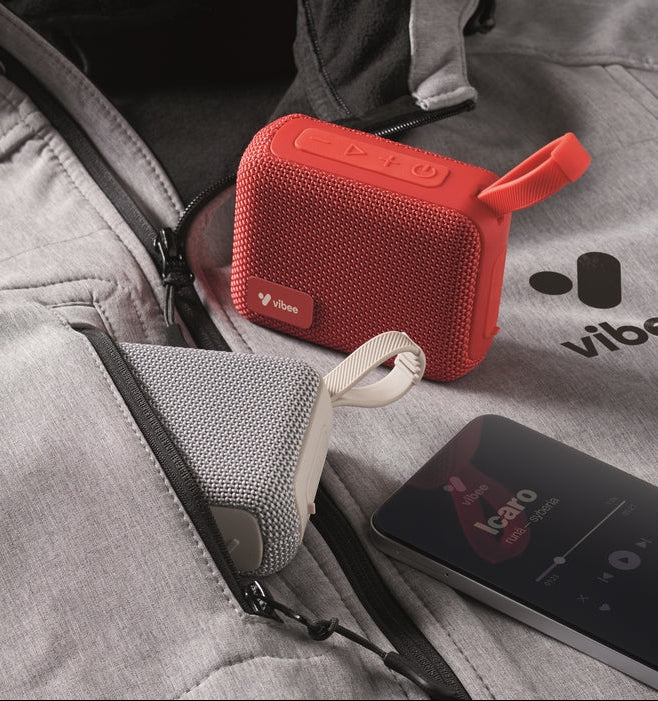 Red portable speaker on a gray surface with a phone displaying music app.