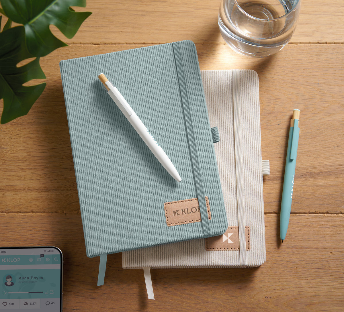 Two notebooks stacked on a wooden surface with a pen and smartphone.
