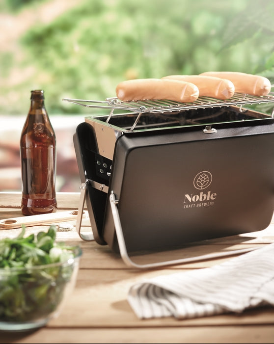 Portable grill with sausages on a wooden table outdoors
