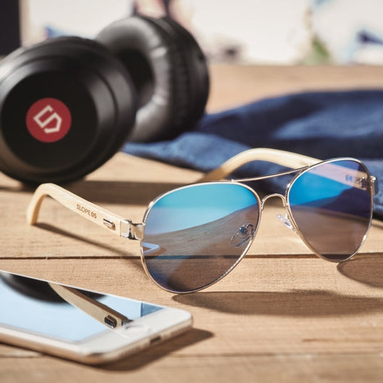 Aviator sunglasses with reflective lenses on a wooden surface with headphones and a phone.