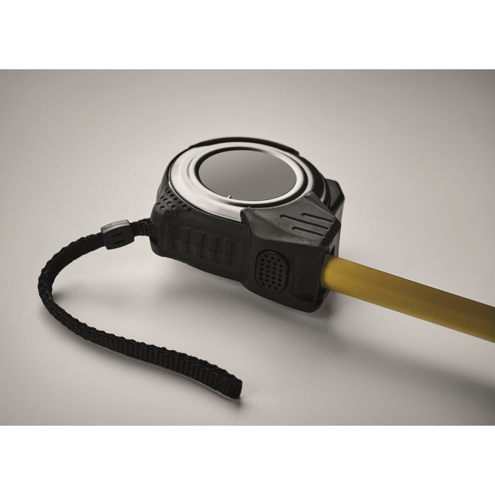 A close-up of a black tape measure with a yellow pull cord, shown on a neutral gray background.