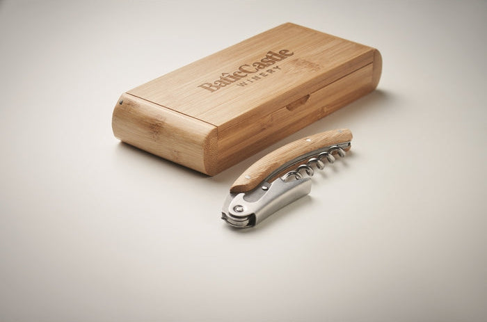 A corkscrew with a light wood handle and silver metal body, placed in front of a rectangular bamboo storage case engraved with the brand name 'Beck & Castle'.