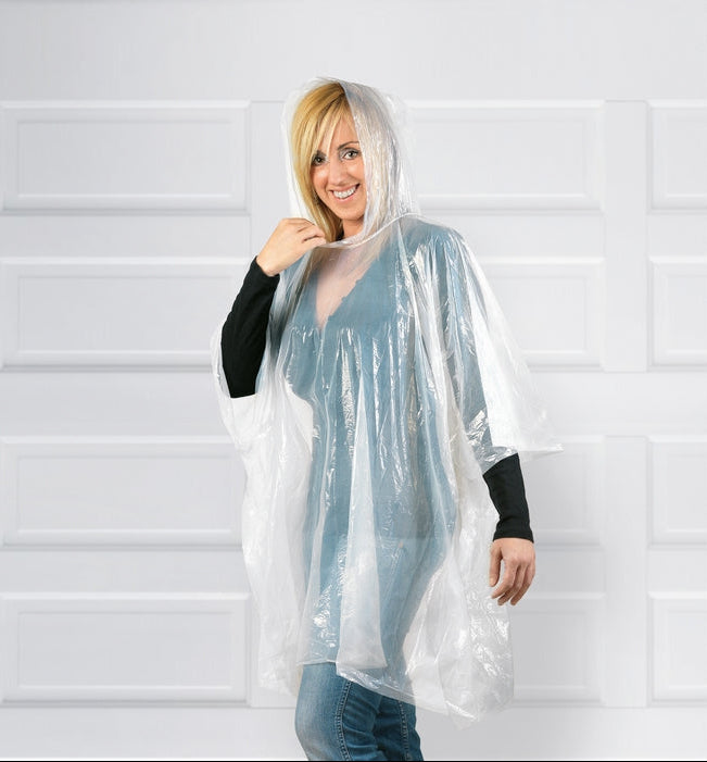 A woman wearing a clear, hooded plastic rain poncho over a blue top and jeans, standing in front of a white paneled garage door.