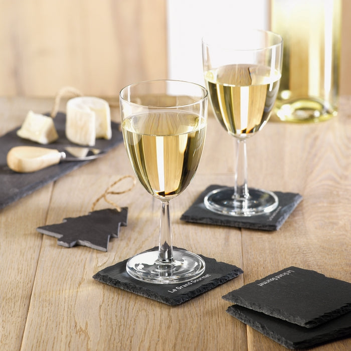 Two wine glasses with white wine on black coasters on a wooden table with cheese and crackers.