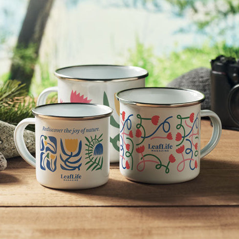 Three decorated mugs on a wooden surface with a camera and natural background