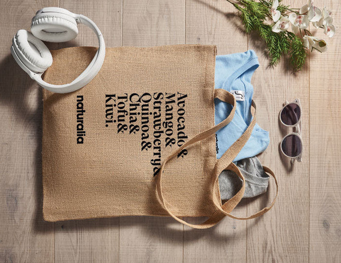 Jute bag with a list of ingredients and 'naturalia' branding on a wooden surface with accessories.